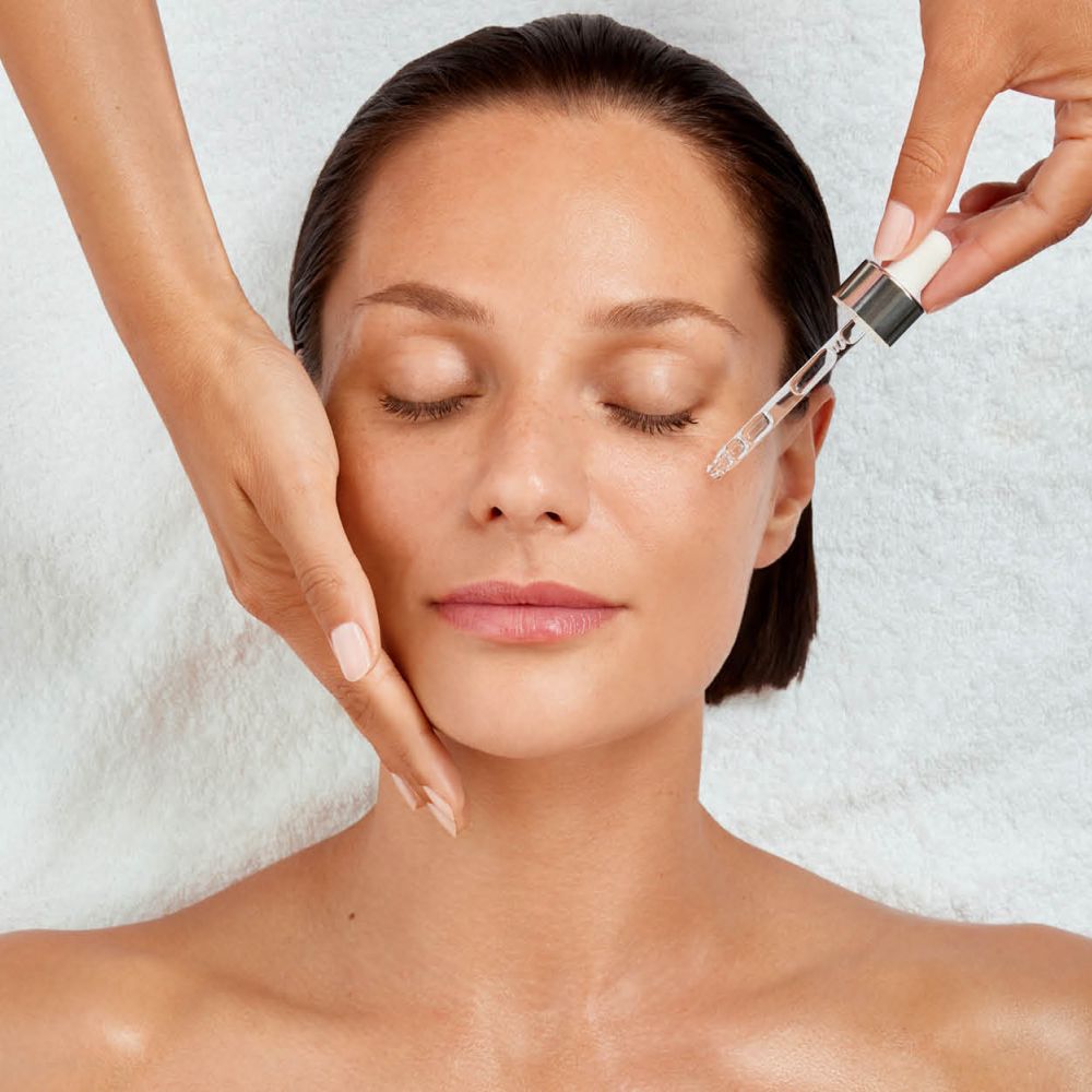 Frau mit geschlossenen Augen, Hand stützt die Wange, Pipette träufelt Serum aufs Gesicht