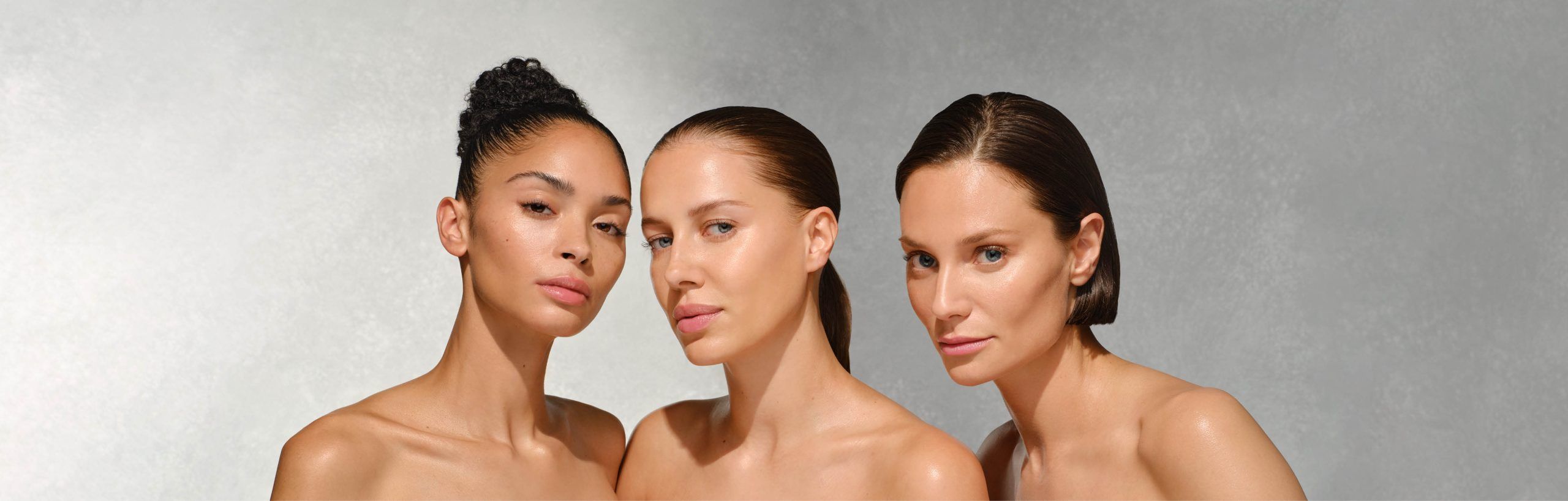 Drei Frauen Schulter an Schulter vor grauem Hintergrund